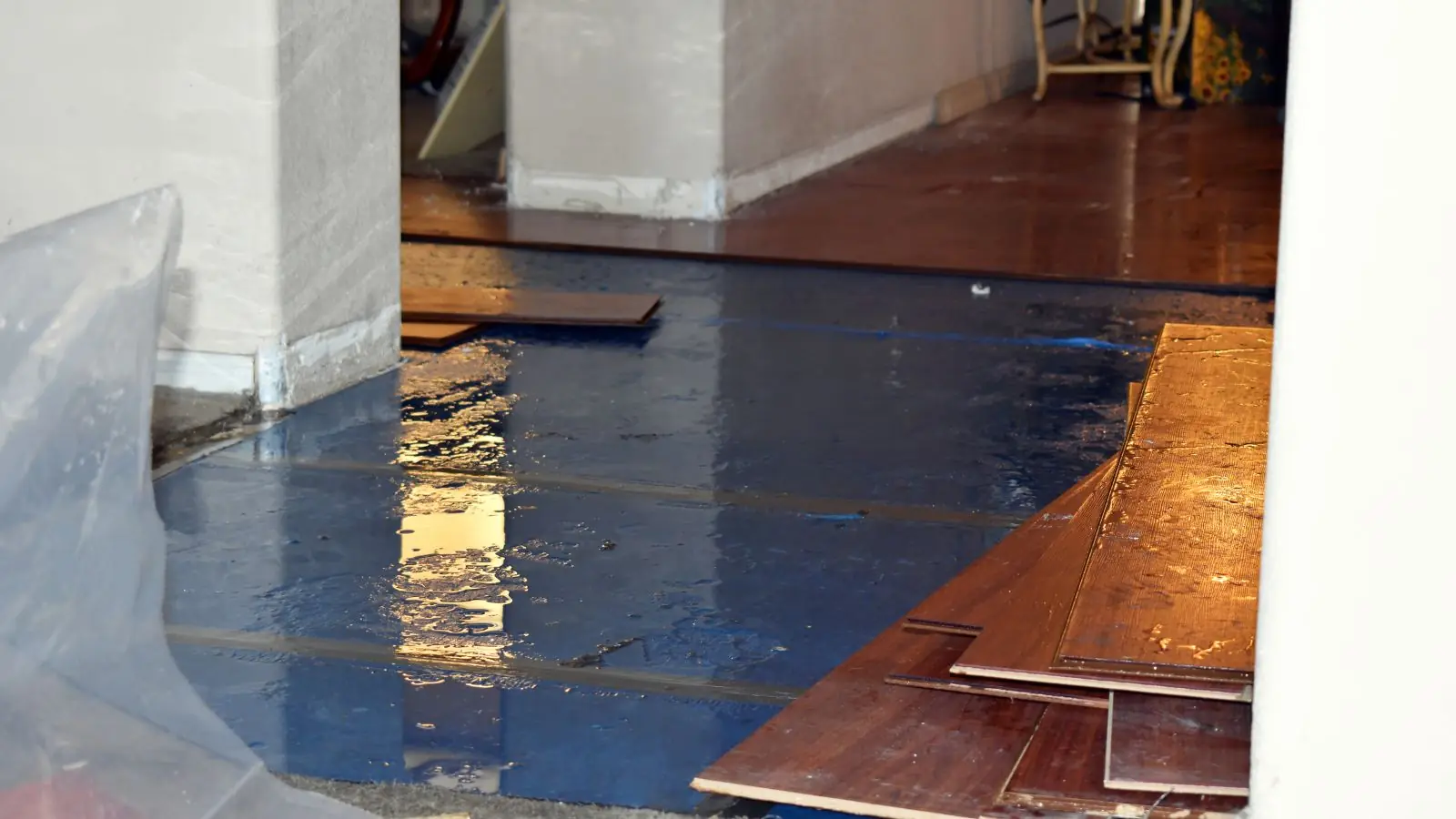 Wood floor boards lifted by water damage with plastic sheeting nearby